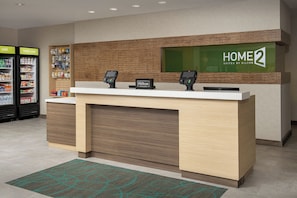 A hotel reception desk with two digital kiosks, a vending machine, and a 'HOME 2' sign. - Home2suites by Hilton Miami Airport S. Blue Lagoon (Miami)