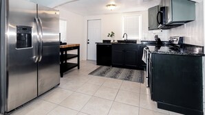 A modern kitchen with stainless steel appliances, black cabinetry, and a tiled floor. - 2-Bedroom Home Away from Home in St Petersburg (St. Petersburg)