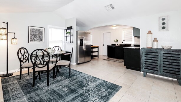 A modern kitchen with a dining area, featuring a stainless steel refrigerator, a dining table with chairs, and a kitchen island with a sink. - 2-Bedroom Home Away from Home in St Petersburg (St. Petersburg)