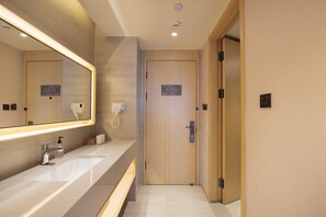 A hotel bathroom with a large mirror, two sinks, a towel dispenser, and a door with a sign.