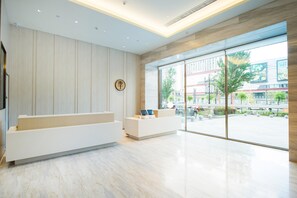 A modern reception area with a wooden panel wall, a reception desk, and a large window offering a view of the street. - Ji Hotel (Jilin)