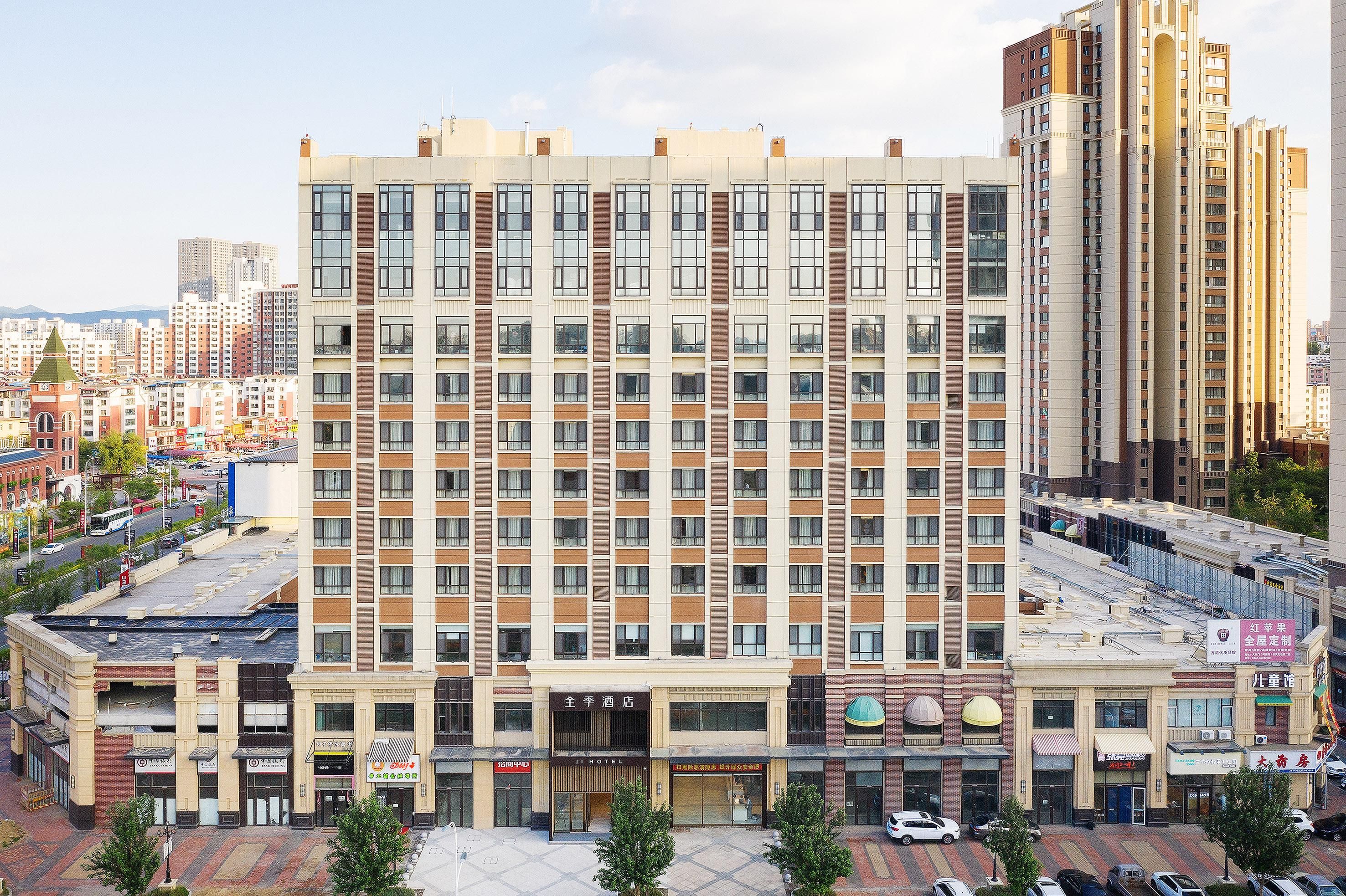 A multi-story hotel with a central entrance, multiple floors, and a parking area in front.