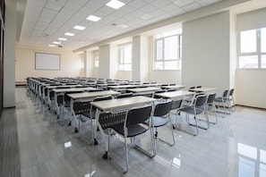 A classroom with rows of desks and chairs, a projector screen, and large windows. - Ji Hotel (Jilin)