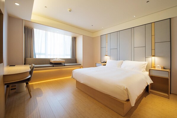 A modern hotel room with a large bed, a desk, and a window with curtains.