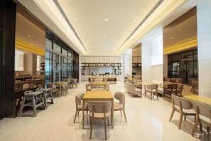 A modern dining area with multiple tables and chairs, a central kitchen area, and large windows.