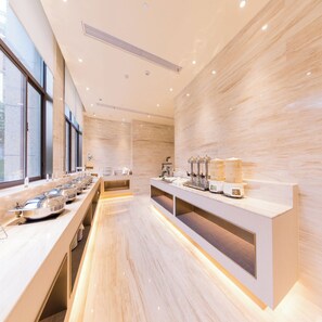 A modern hotel kitchen with a long counter, stainless steel appliances, and a view through the windows.
