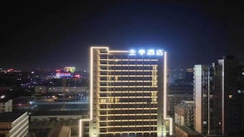 A multi-story hotel with a prominent illuminated sign, a parking area, and surrounding urban buildings.