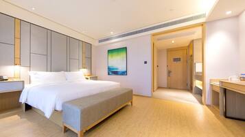A hotel room with a bed, bedside table, bench, artwork, and a door leading to a bathroom.