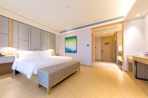 Quarto de hotel com cama, mesa de cabeceira, um banco, obra de arte e porta para o banheiro.