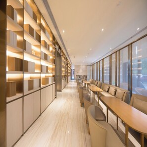 A modern hotel lobby with a long reception desk, seating area, and a wall with illuminated shelves.
