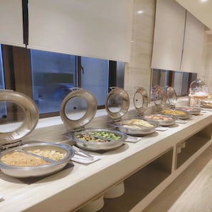 A buffet setup with various food items in covered containers. - Ji Hotel (Hefei)
