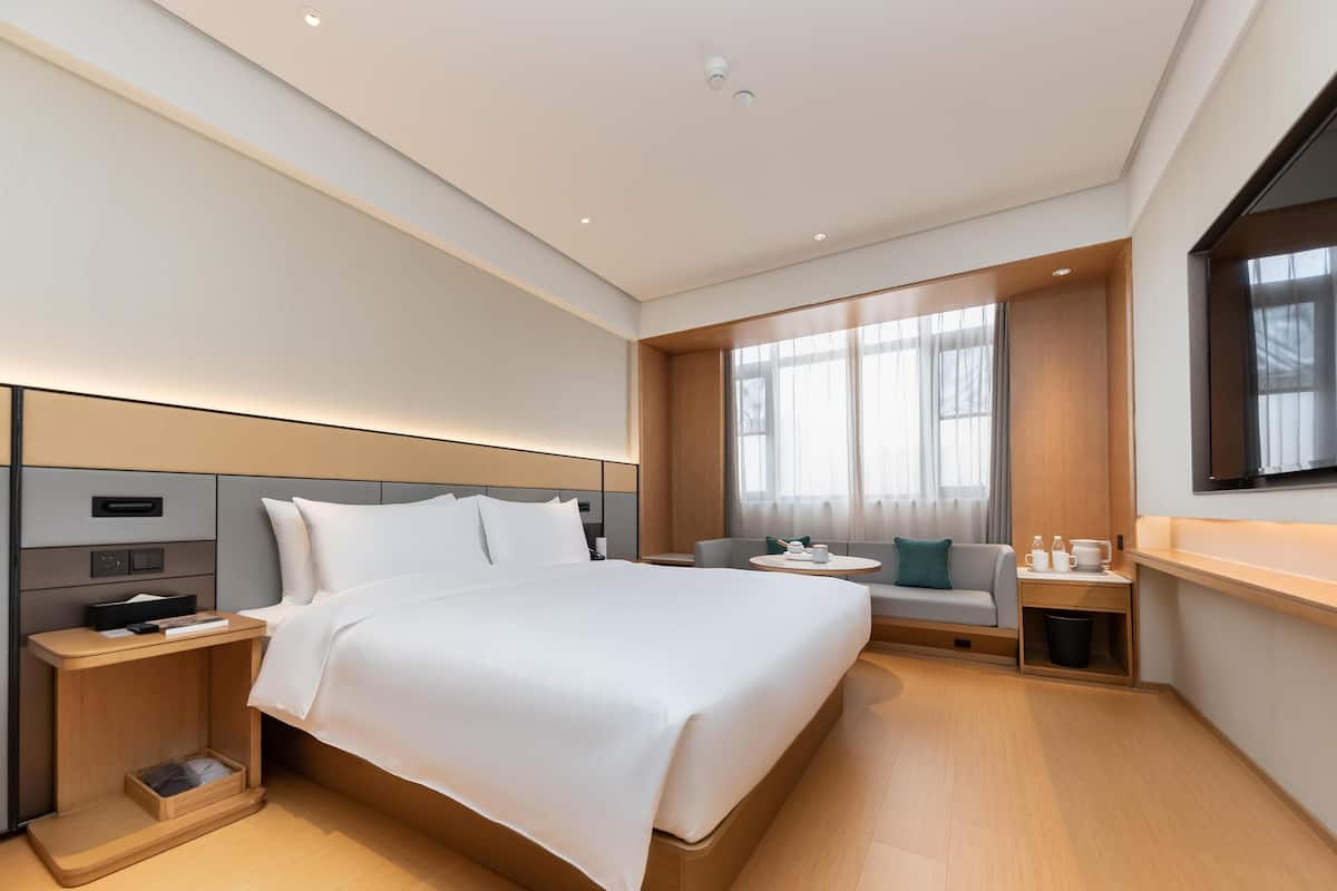 Una camera d'albergo moderna con un letto grande, comodini, una zona salotto e un'ampia finestra.