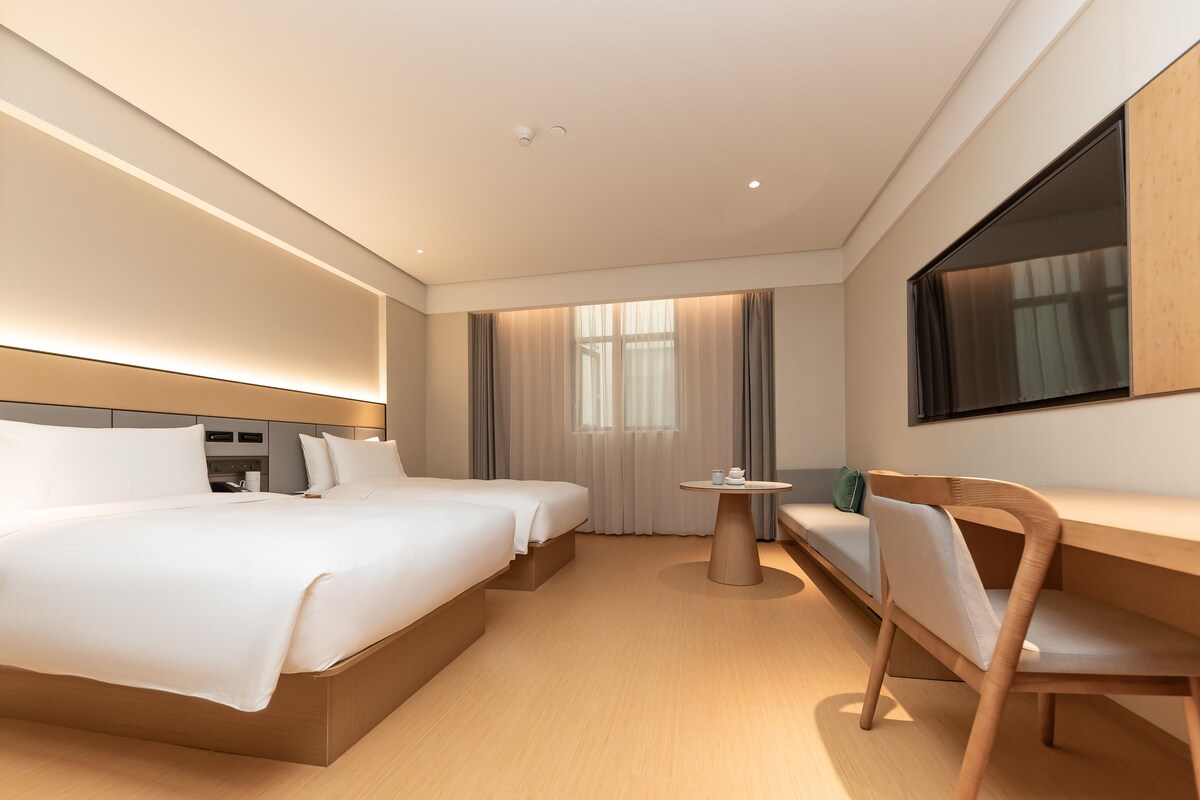 A hotel room with a large bed, a desk, a chair, a TV, and a window with curtains.
