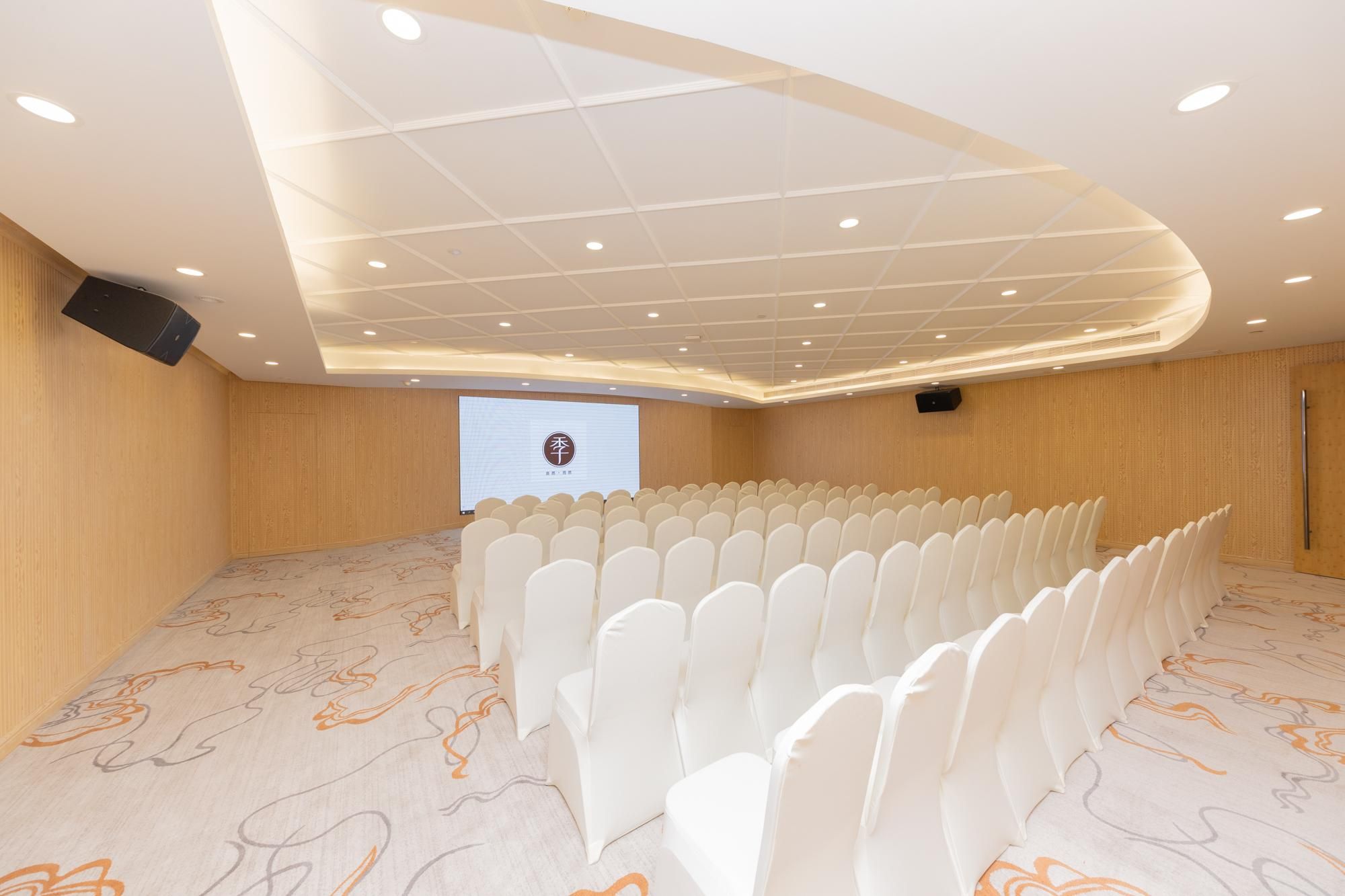 A conference room with rows of white chairs, a projector screen, and a patterned carpet.