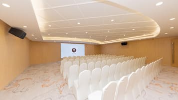 A conference room with rows of white chairs, a projector screen, and a patterned carpet.
