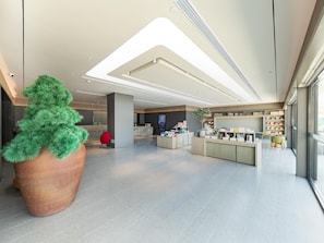 A modern lobby with a large potted plant, a reception desk, and a television screen. - Ji Hotel (Nanjing)