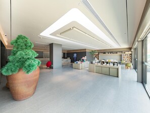 A modern lobby with a large potted plant, a reception desk, and a television screen. - Ji Hotel (Nanjing)