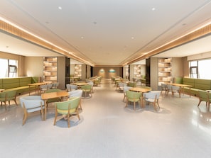 A spacious library with rows of tables and chairs, bookshelves, and a central decorative feature. - Ji Hotel (Nanjing)