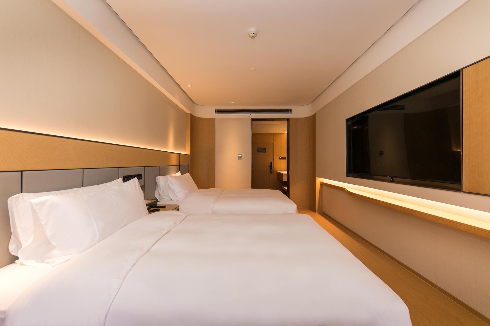 Quarto de hotel com duas camas, uma televisão grande e um banheiro visível através de uma porta aberta.