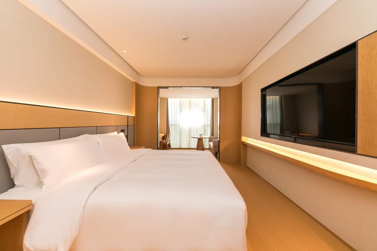 Habitación de hotel con una cama grande, un televisor montado en la pared y un escritorio con una silla.