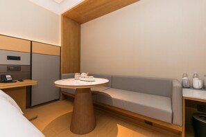 A modern hotel room with a round wooden table, a gray sofa, and a small desk with a telephone.