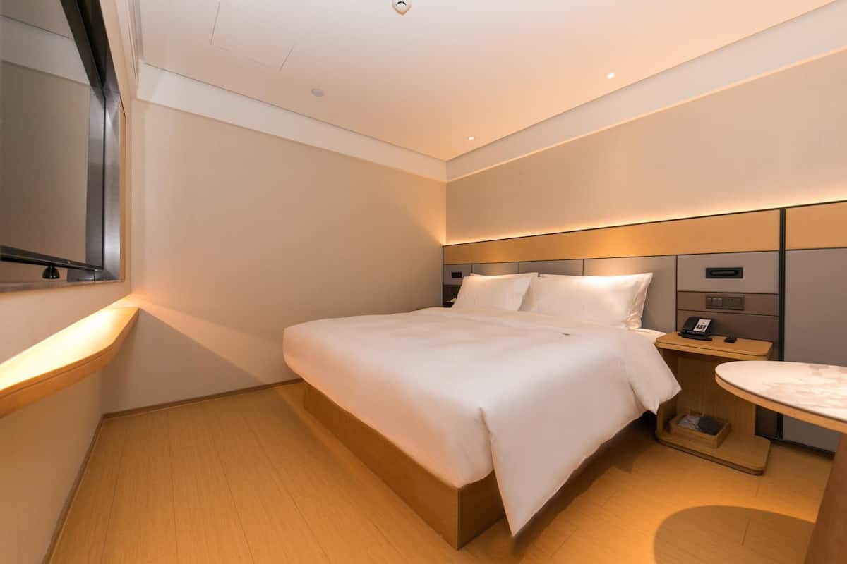 Una habitación de hotel moderna con una cama grande, una mesita de noche y una pequeña mesa redonda.