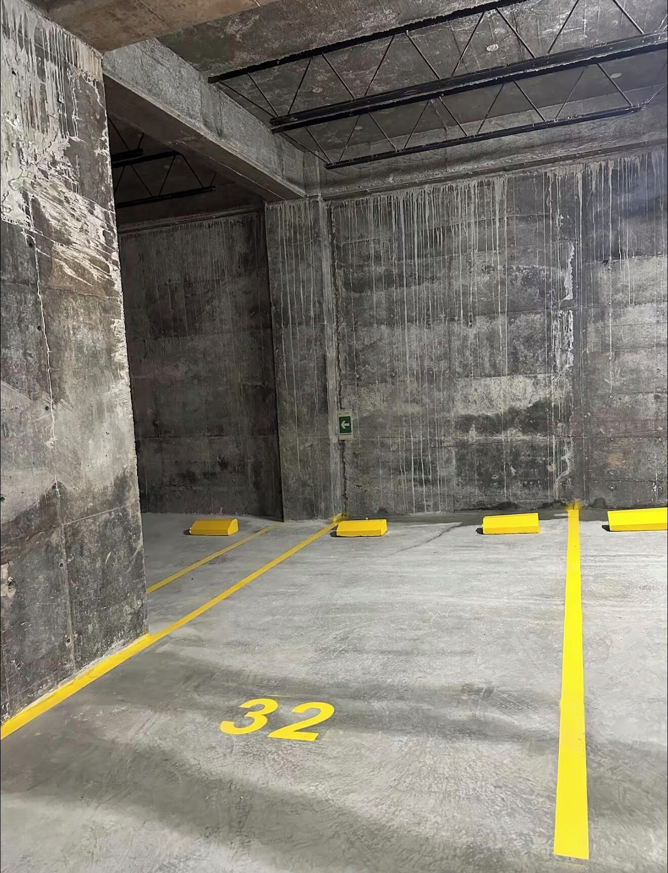 Eine Parkgarage mit Betonwänden, gelben Markierungen für Parkplätze und einem grünen Hinweisschild für den Ausgang.