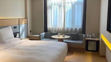 A hotel room with a large bed, a sofa, a small table, and a window with curtains.