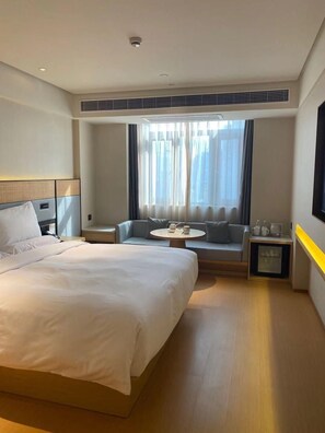 A hotel room with a large bed, a sofa, a small table, and a window with curtains. - Ji Hotel (Shanghai)