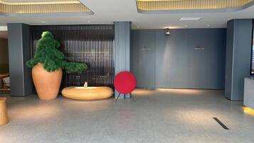 A modern lobby with a large potted plant, a red circular seating area, and a reception desk.