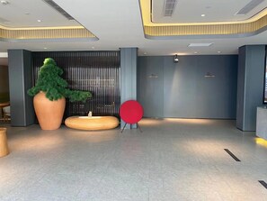 Un vestíbulo moderno con una gran planta en maceta, una zona de estar circular roja y un mostrador de recepción.