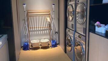 A laundry room with a drying rack, two washing machines, and a vacuum cleaner.