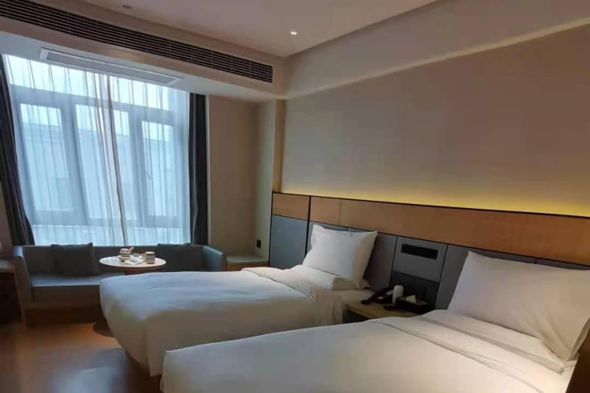 A hotel room with two beds, a sofa, a small table, and a window with curtains.