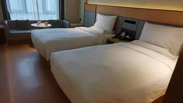 A hotel room with two beds, a sofa, a small table, and a window with curtains.