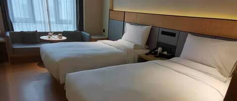 A hotel room with two beds, a sofa, a small table, and a window with curtains.