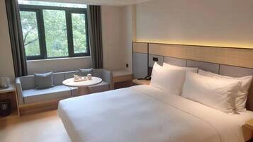 A hotel room with a large bed, a sofa with a table, and a window with curtains.