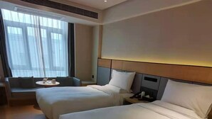 Habitación de hotel con dos camas, un sofá, una mesita y una ventana con cortinas.