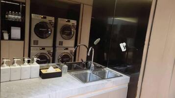 A modern kitchen with a marble countertop, stainless steel sink, and a row of washing machines in the background.