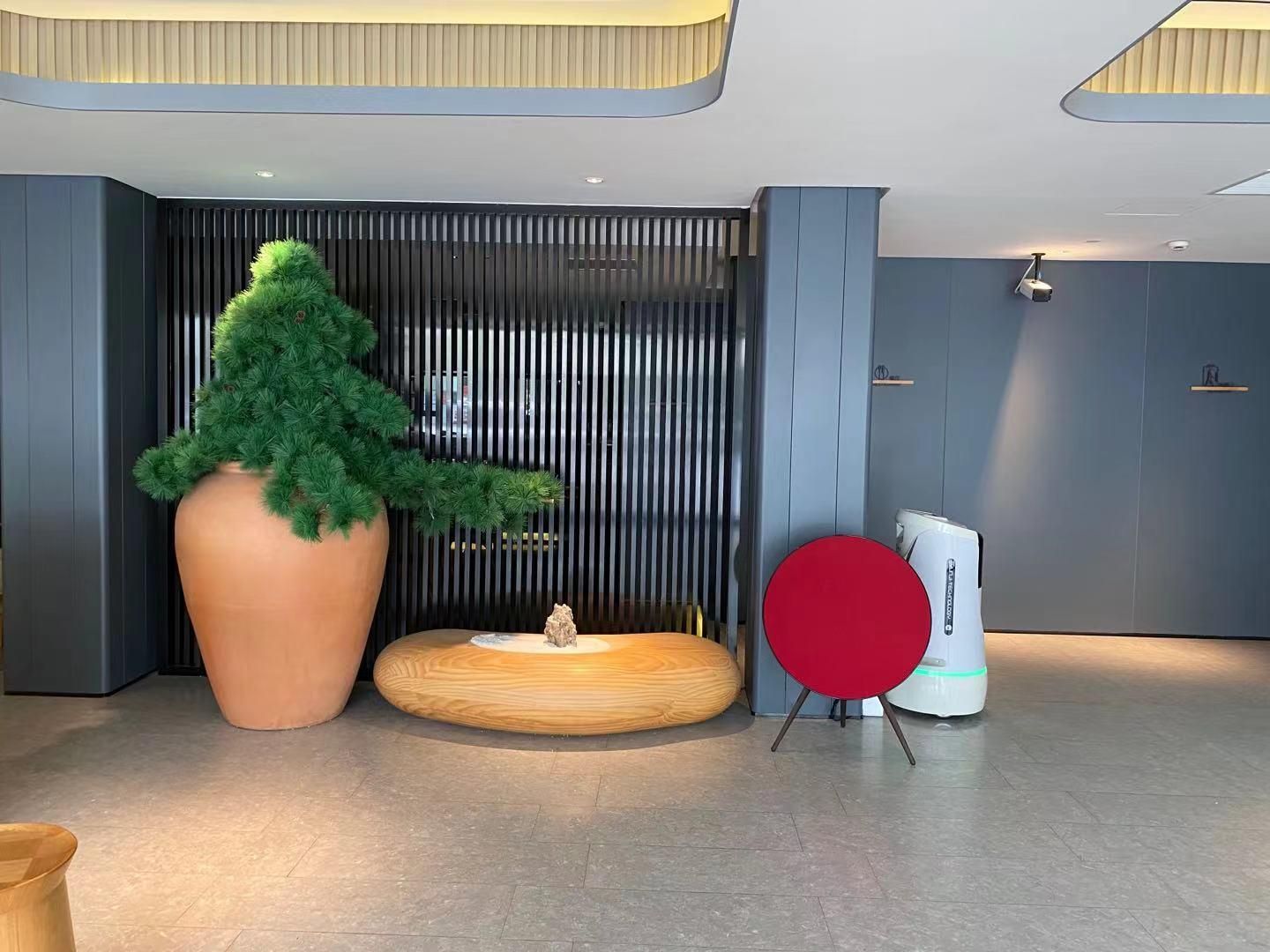 A modern lobby with a large potted tree, a round wooden table, and a red chair.