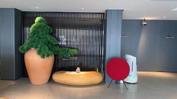 A modern lobby with a large potted tree, a round wooden table, and a red chair.