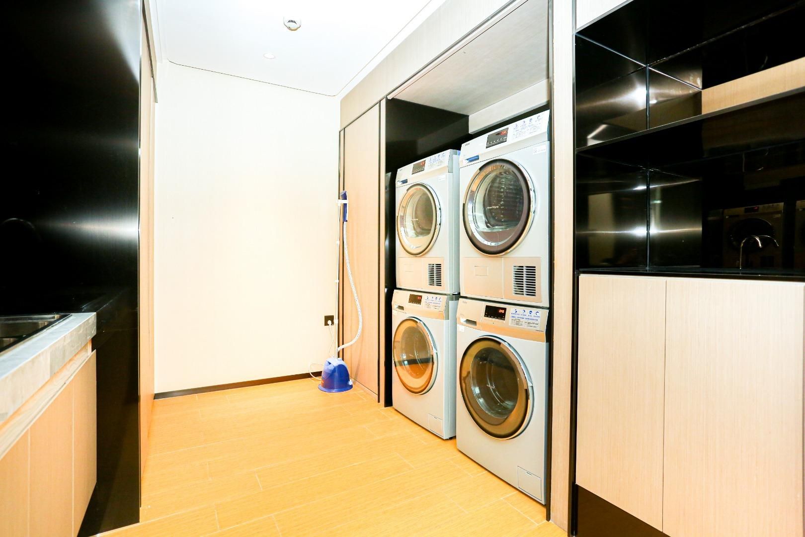 A laundry room with stacked washing machines, a blue vacuum cleaner, and wooden cabinets.