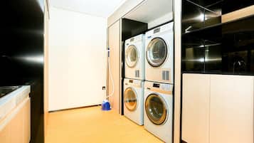 A laundry room with stacked washing machines, a blue vacuum cleaner, and wooden cabinets.
