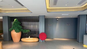 Un vestíbulo moderno con una gran planta en maceta, una zona de estar circular roja y un mostrador de recepción.