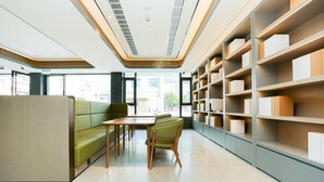 Una biblioteca moderna con un sofá verde, mesas de madera y estanterías.