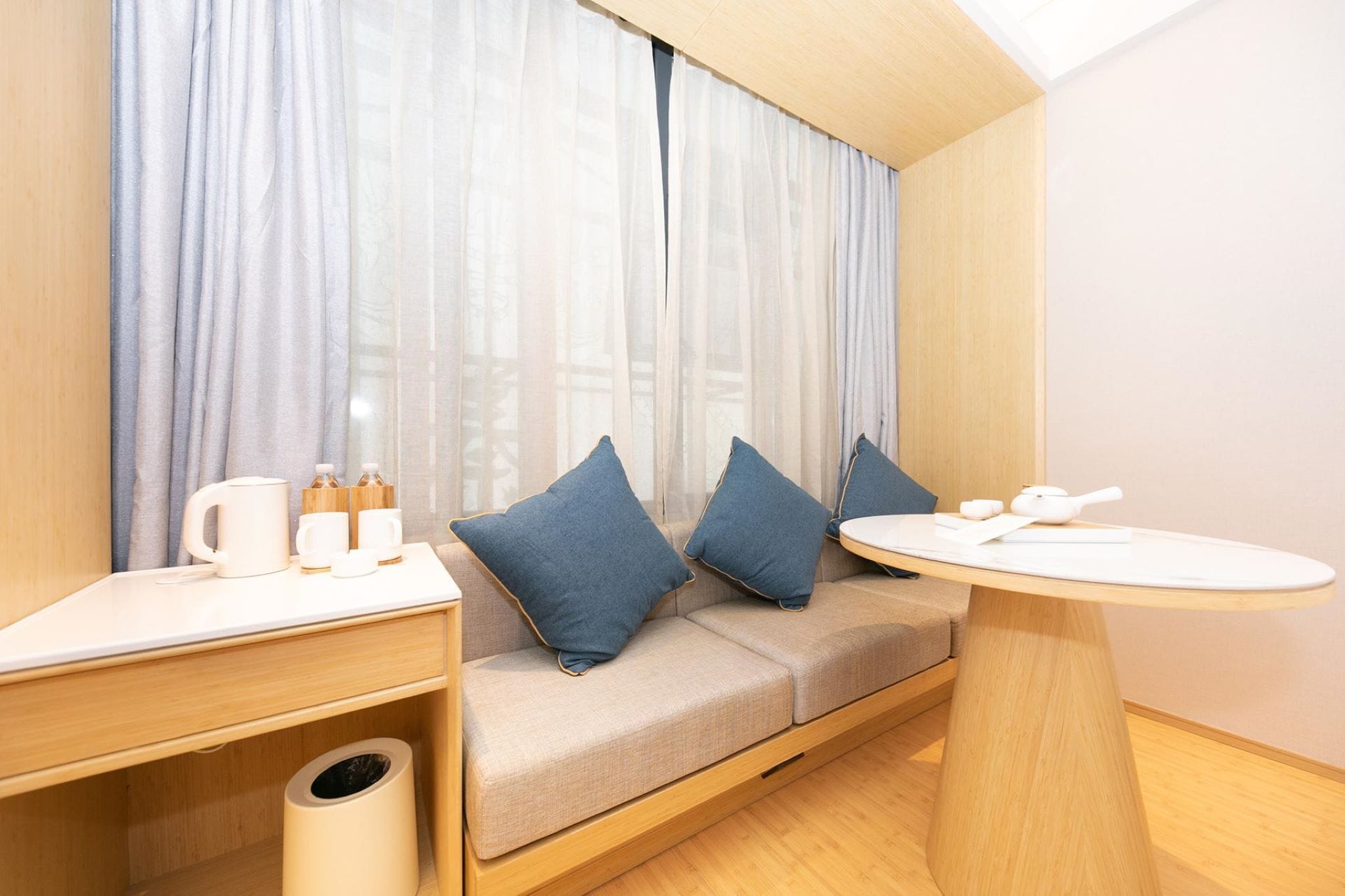 A modern room with a sofa, a small table, and a window with sheer curtains.
