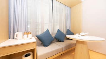 A modern room with a sofa, a small table, and a window with sheer curtains.