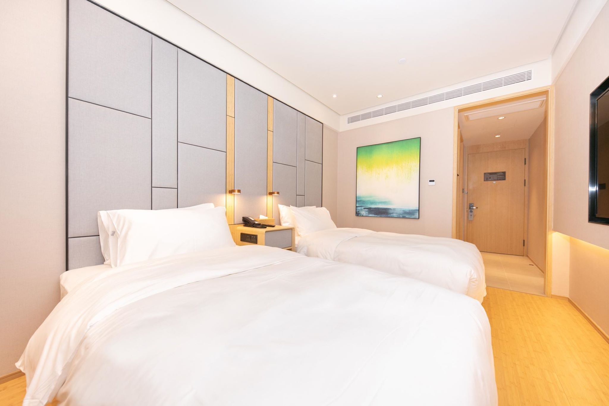 A hotel room with two beds, a nightstand, a painting, and a door leading to another room.