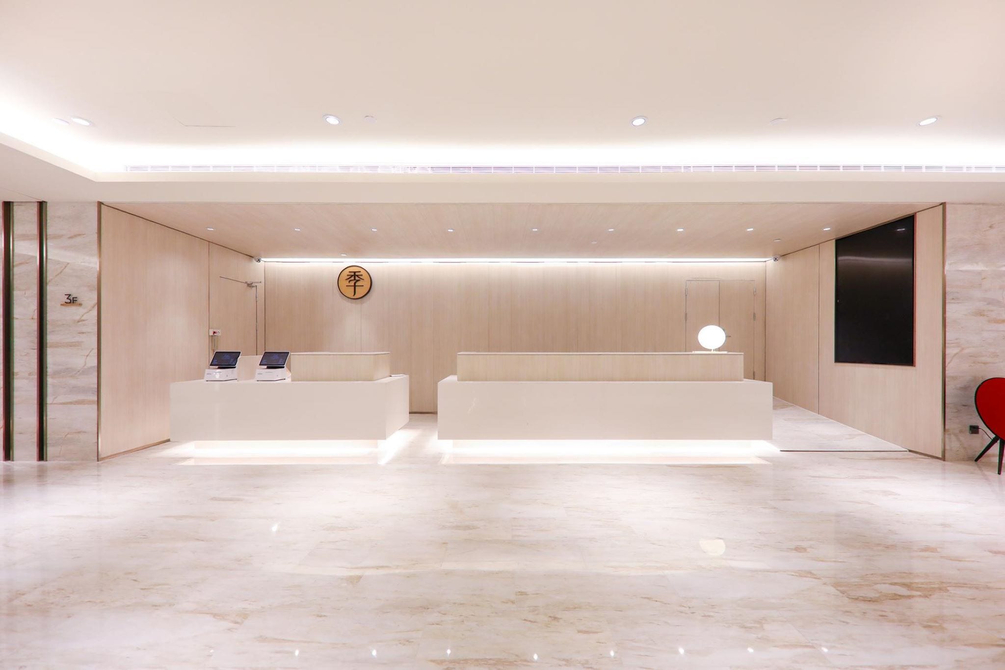 A modern reception area with a marble floor, two reception desks, a wall-mounted clock, and a red chair.