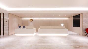 A modern reception area with a marble floor, two reception desks, a wall-mounted clock, and a red chair.