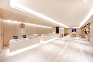 A modern hotel reception area with a wooden reception desk, digital displays, a seating area, and a view of the city. - Ji Hotel (nanjing Confucius Temple Pedestrian Stre (Nanjing)